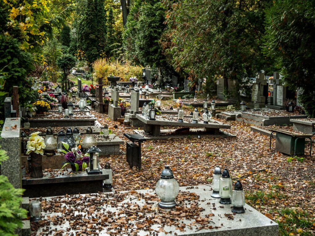 Peaceful cemetery in autumn with fallen leaves and lanterns on graves adding a serene atmosphere.
